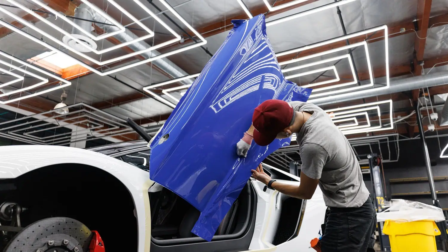 Installer fitting blue wrap vinyl to a car door in a brightly lit shop